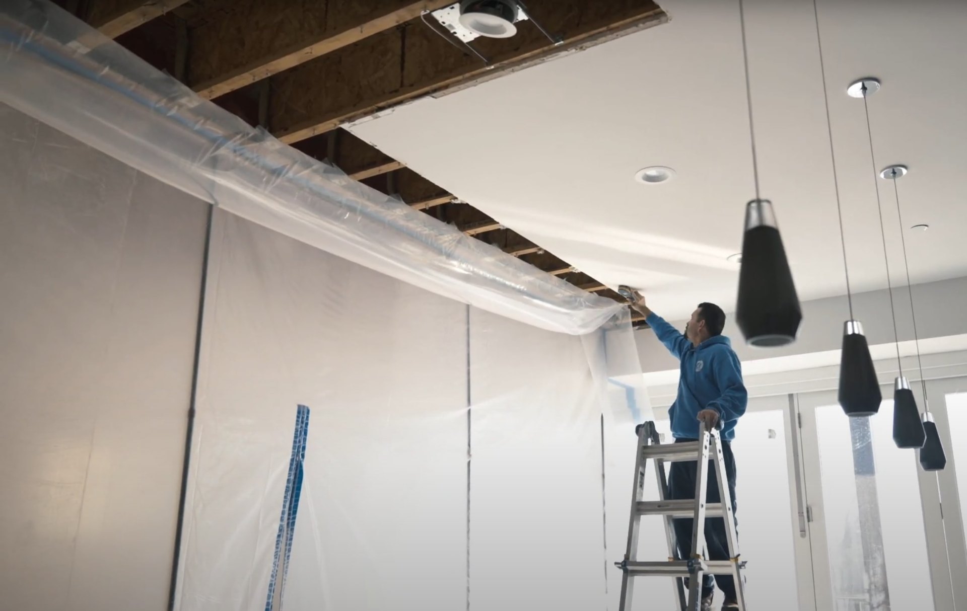 Commercial water damage restoration and ceiling repair services Professional water damage restoration technician working on ceiling repair with plastic sheeting and ladder in commercial space