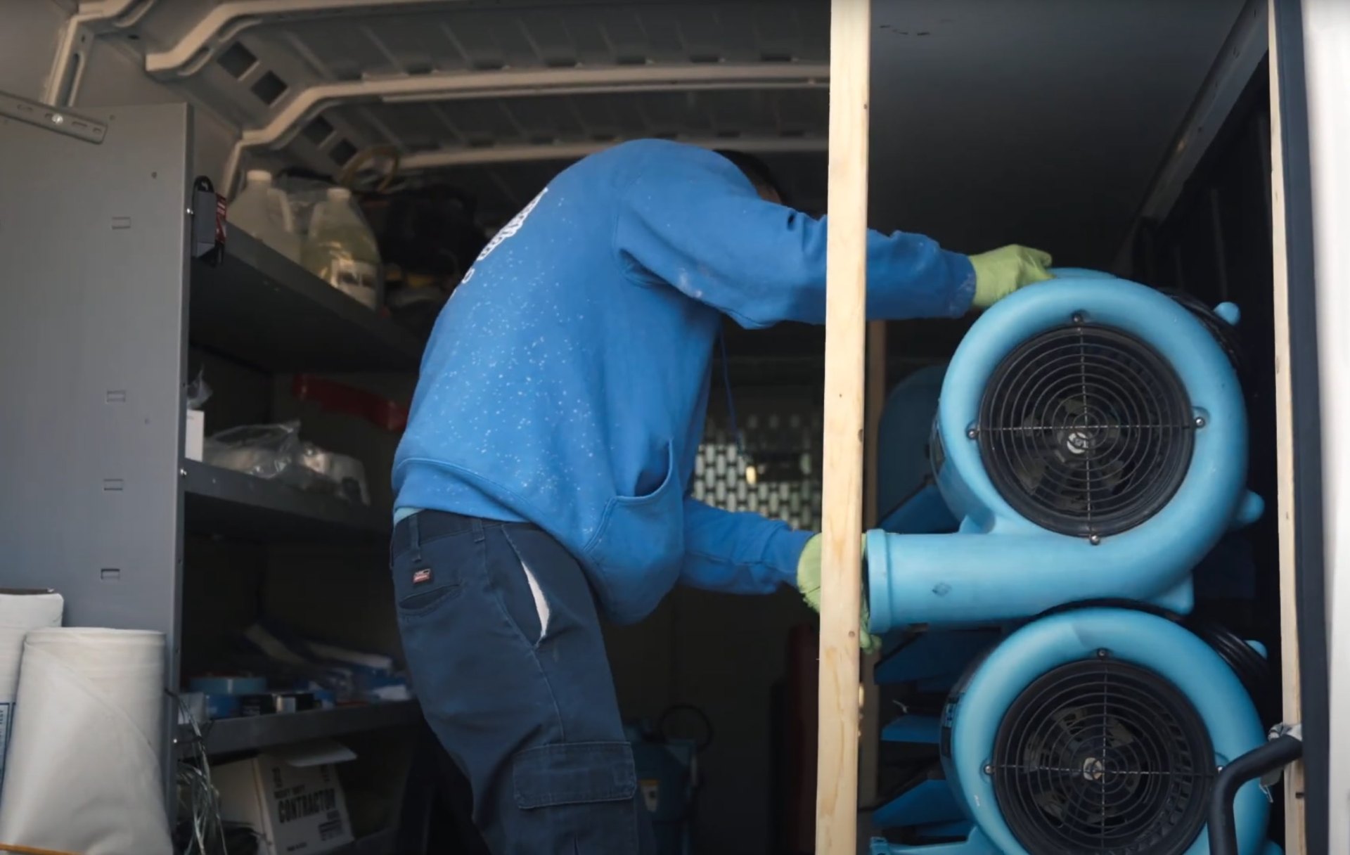Professional water damage restoration equipment and mold prevention services Professional water damage restoration technician in protective gear working with industrial drying equipment and blue air movers